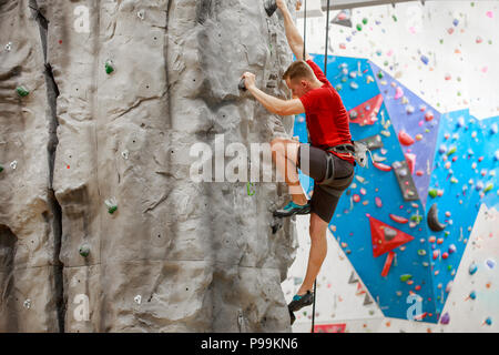 Photo de côté de sports type en T-shirt rouge de la formation sur le mur d'escalade intérieur Banque D'Images