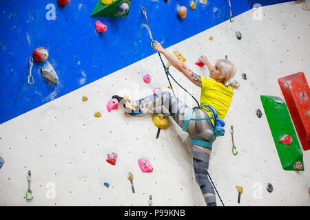 Photo de l'arrière de la jeune fille ahtlete en jaune T-shirt brouille sur mur d'escalade à workout Banque D'Images