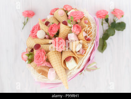 Bouquet composé de fleurs de roses, cônes alvéolés, des bonbons et des guimauves sur un léger fond de bois Banque D'Images