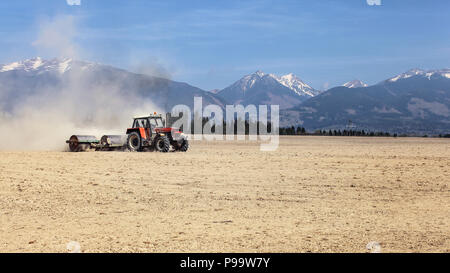 Le tracteur tirant sur les rouleaux de métal avec les montagnes en arrière-plan. Préparation du sol au printemps. Banque D'Images