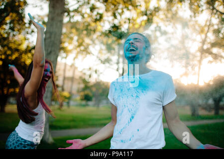 Beau jeune couple jouant avec les peintures colorées dans le parc. L'homme et la femme s'amusant de temps à l'extérieur sur le color festival. Banque D'Images