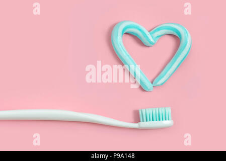 Des brosses à dents et dentifrice de couleur turquoise en forme de coeur sur fond rose. Soins dentaires et de concept. Banque D'Images