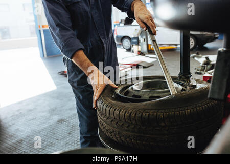 Cropped shot de mécanicien de retirer le pneu de la jante sur la machine. Les mains du technicien de l'extraction de la roue de l'automobile de rim. Banque D'Images
