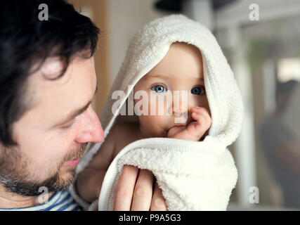 Père avec un tout-petit enfant enveloppé dans une serviette de bain à la maison. Banque D'Images