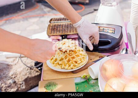 La cuisson des gaufres gaufrier en fer. L'homme avait les mains avec gaufres Banque D'Images