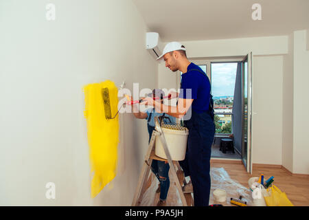 Mâle et femelle avec bâton de peinture au rouleau et pinceau leur coloration jaune dans la chambre Banque D'Images