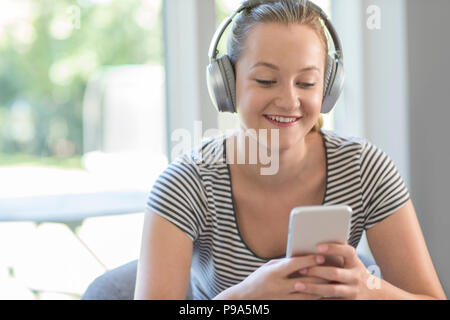 Femme à la maison d'eau de la musique à partir d'un téléphone portable sur un casque sans fil Banque D'Images