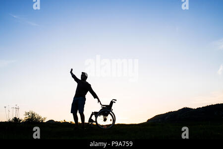 Un jeune homme debout en fauteuil roulant dans la nature dans la soirée. Banque D'Images