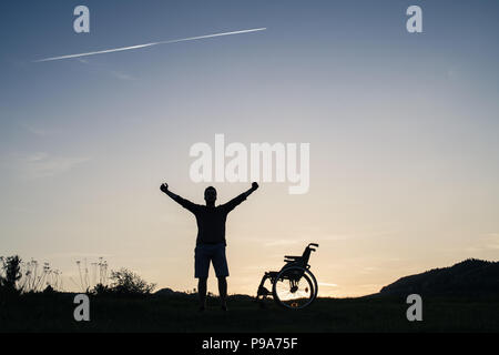 Un jeune homme debout en fauteuil roulant dans la nature dans la soirée. Banque D'Images