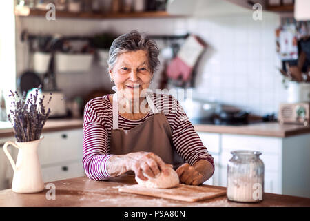 A senior woman kneading dough dans la cuisine à la maison. Banque D'Images