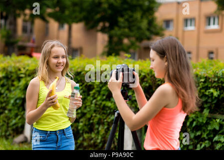 Deux filles lycéenne. À l'été en ville. Écrit la vidéo à l'appareil photo. Dans les mains est titulaire des bananes et une bouteille d'eau. Le concept d'un blog vidéo sur l'alimentation saine. Banque D'Images