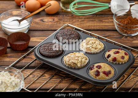 Muffins dans différents ou de cuisson moules à muffin sur broun fond de bois. Recette de muffins de base. Des muffins pour le petit déjeuner ou un dessert. Banque D'Images