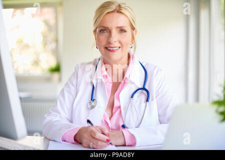Close-up portrait of senior female doctor sitting at cabinet de médecin à 24 en face de l'ordinateur portable et faire quelques formalités administratives. Banque D'Images