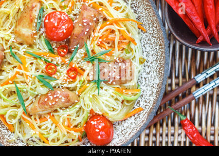 Nouilles sautées au poulet, légumes (carotte, tomate, courgette, ail, poivron rouge, oignon vert), graines de sésame et de sauce de soja sur la plaque d'argile fermer Banque D'Images