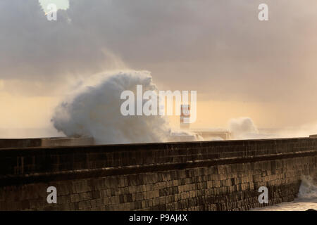 De fortes vagues se briser contre pier avec intéressant fin de journée lumière filtre à travers les nuages et l'humidité. Porto, Portugal, en janvier. Banque D'Images