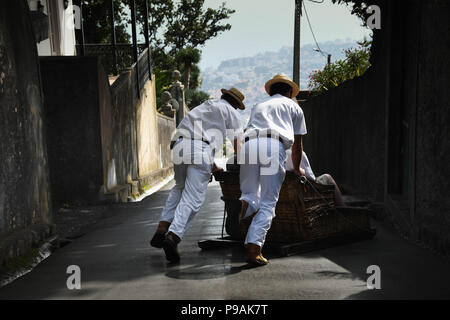 Les touristes appréciant un tour en descente sur un toboggan traditionnel panier en osier dans la rue au-dessus de Funchal, Madeira Island Banque D'Images