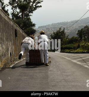Les touristes appréciant un tour en descente sur un toboggan traditionnel panier en osier dans la rue au-dessus de Funchal, Madeira Island Banque D'Images