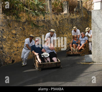 Les touristes appréciant un tour en descente sur un toboggan traditionnel panier en osier dans la rue au-dessus de Funchal, Madeira Island Banque D'Images