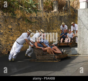 Les touristes appréciant un tour en descente sur un toboggan traditionnel panier en osier dans la rue au-dessus de Funchal, Madeira Island Banque D'Images