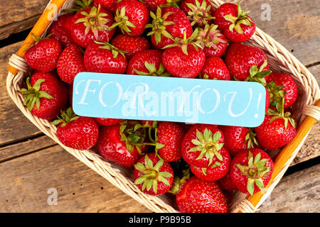 Panier rempli de frais jardin les fraises. Fraises Juteuses mûres dans panier sur le vieux fond de bois. Frais de ferme. Banque D'Images