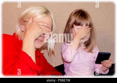 Belle blonde jeune grand-mère et petite-fille cute peu fermer les yeux avec les mains Banque D'Images