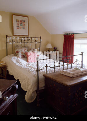 Couette blanche sur lit en laiton vintage cottage chambre avec un coffre en bois peint au pied du lit Banque D'Images