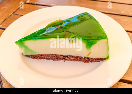 Tranche triangulaire de vitrage vert flan doux gâteau sur une base de biscuit brun servis sur une plaque ronde blanche sur une table woode Banque D'Images