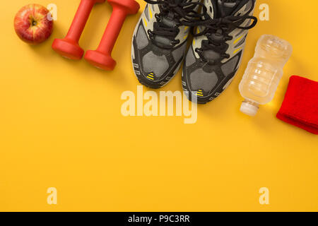 Les chaussures de sport, des haltères, apple, une bouteille d'eau et bandes de poignet. Still Life Fitness, sur fond jaune avec copie espace. Banque D'Images