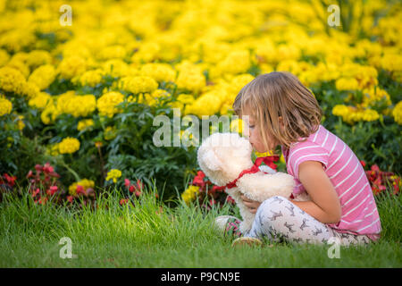 Adorable girl kissing her favourite ours en parc d'été sur belle journée ensoleillée avec des fleurs jaunes à l'arrière-plan Banque D'Images