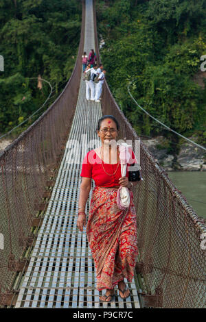 Femme traversant une rivière sur un pont suspendu au Népal Banque D'Images