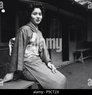 Années 1950, historiques, une jeune femme assise à l'extérieur portant un kimono traditionnel japonais, l'habillement femelle, appelé "costume national ome du Japon'. Banque D'Images