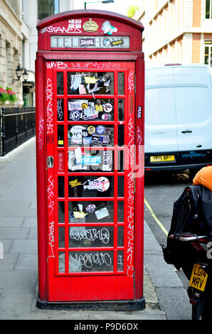 Boîte de téléphone rouge traditionnels couverts de graffitis et autocollants, centre de Londres, Angleterre, Royaume-Uni. Banque D'Images