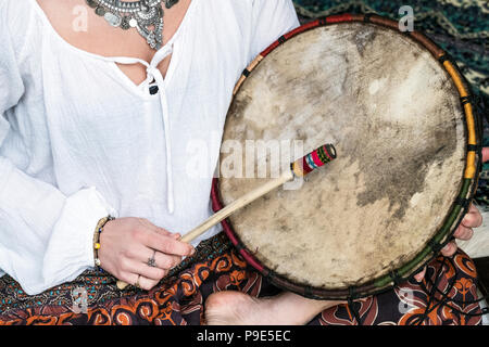 Portrait de femme portant un pantalon à motif floral assis sur des tapis, holding shaman tambour. Banque D'Images