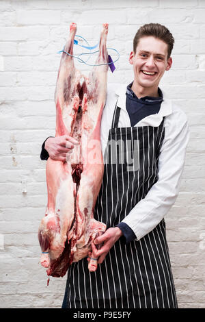 Un boucher tenant une carcasse de viande d'agneau préparé complet pour couper en petits joints pour la vente. Banque D'Images