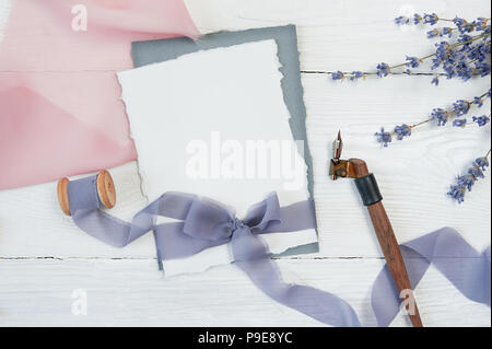 Carte vierge blanc ribbon bow sur fond de tissu bleu et rose avec des fleurs de lavande et Plume calligraphique sur un fond blanc. Immersive avec enveloppe et carte vierge. Mise à plat. Vue d'en haut Banque D'Images