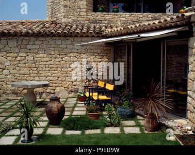 Chaises jaune sur une terrasse pavée de villa méditerranéenne avec un auvent blanc au-dessus de portes de patio Banque D'Images