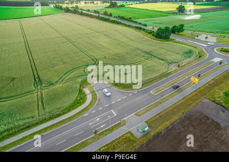 Vue aérienne d'une route avec des signes et des lignes directrices pour le trafic entre une nouvelle zone de développement pour une zone industrielle et une zone de terres arables avec whea vert Banque D'Images