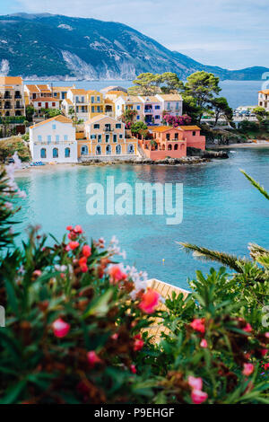 Belles maisons du sud coloré bleu et baie de la mer Méditerranée avec des fleurs rouges sur le premier plan. Village d'Assos à Kefalonia, Grèce Banque D'Images