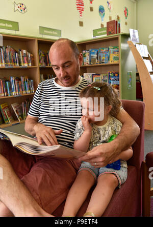 Père de la lecture à sa fille dans bibliothèque pour enfants, Haslemere, Surrey, UK. Samedi 14 juillet 2018. Banque D'Images