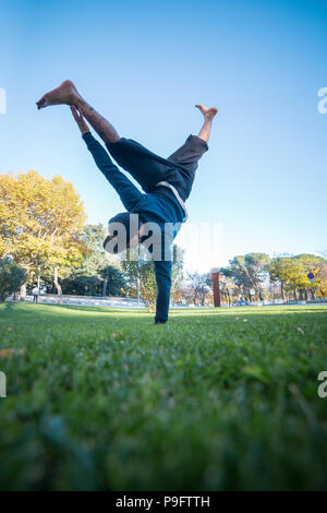 Young man doing handstand sur l'herbe dans la rue en faisant parkour. Banque D'Images