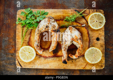 Deux morceaux de poisson grillé avec des tranches de citron et d'herbes le persil sur la coupe de bois, vue du dessus Banque D'Images