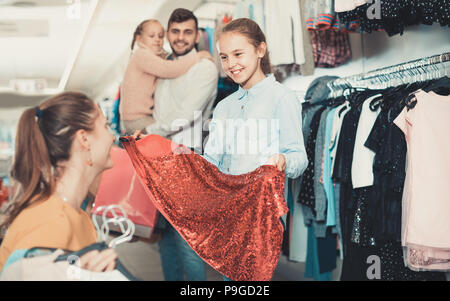 Smiling happy cheerful girl avec la mise en place nouvelle robe en boutique alors que père avec sœur debout derrière Banque D'Images