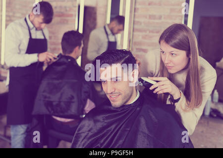 Femme coiffure la coupe de cheveux de clients masculins avec electric clipper en coiffure Banque D'Images