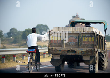 Un homme sur une bicyclette est titulaire sur un camion qui passe, à Delhi, Inde Banque D'Images