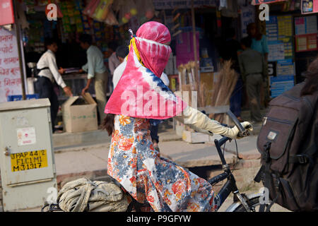 Des scènes de rue de la vraie vie à Delhi en Inde, photographié d'un véhicule en mouvement. Une femme passe par sur un vélo avec la tête entièrement couverte d'une burka rose Banque D'Images