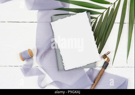 Carte de voeux vierge blanc ruban sur un fond de toile bleue avec la feuille de palmier et Plume calligraphique sur un fond blanc. Immersive avec enveloppe et carte vierge. Mise à plat. Vue d'en haut Banque D'Images