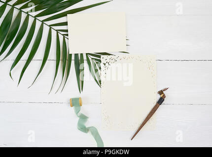 Carte de voeux vierge blanc ruban sur un arrière-plan avec la feuille de palmier et Plume calligraphique sur un fond de bois blanc. Immersive avec enveloppe et carte vierge. Mise à plat. Vue d'en haut Banque D'Images