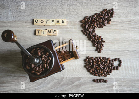 Coffee time citer mot avec les grains de café torréfiés placée sous la forme d'une tasse et soucoupe sur fond de bois, avec broyeur de bois vintage Banque D'Images