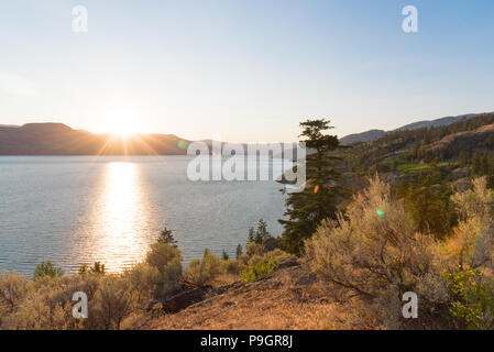 Vue sur le lac Okanagan à partir du Naramata Bench à North en direction de Kelowna, avec soleil derrière les montagnes Banque D'Images