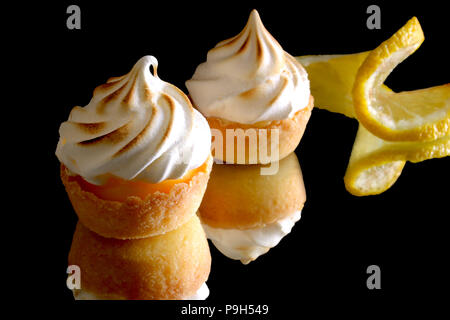 Mini tartelettes au citron meringuée sur un fond réfléchissant noir Banque D'Images